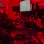 two men sitting at a desk in front of computer monitors